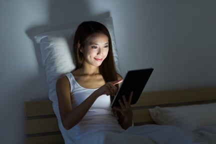 Woman working overnight with tablet pc and sitting on bed